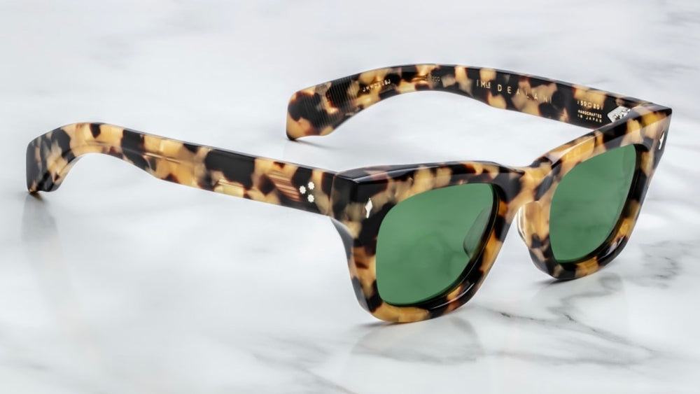 Side veiw Jacques Marie Mage Dealan Gold Dust sunglasses featuring bold, square 10 mm cured acetate frames in a speckled honey‑and‑caramel ‘Gold Dust’ pattern. Sterling‑silver arrowhead front pins and spur‑shaped rivets accent the temples, which house hidden silver wire‑core reinforcements and custom 7‑barrel hairline hinges. The demo lenses are Highland‑green CR39 with backside anti‑reflective coating, offering full UV protection. Handcrafted in Japan limited‑edition release, inspired by vintage Japanese a
