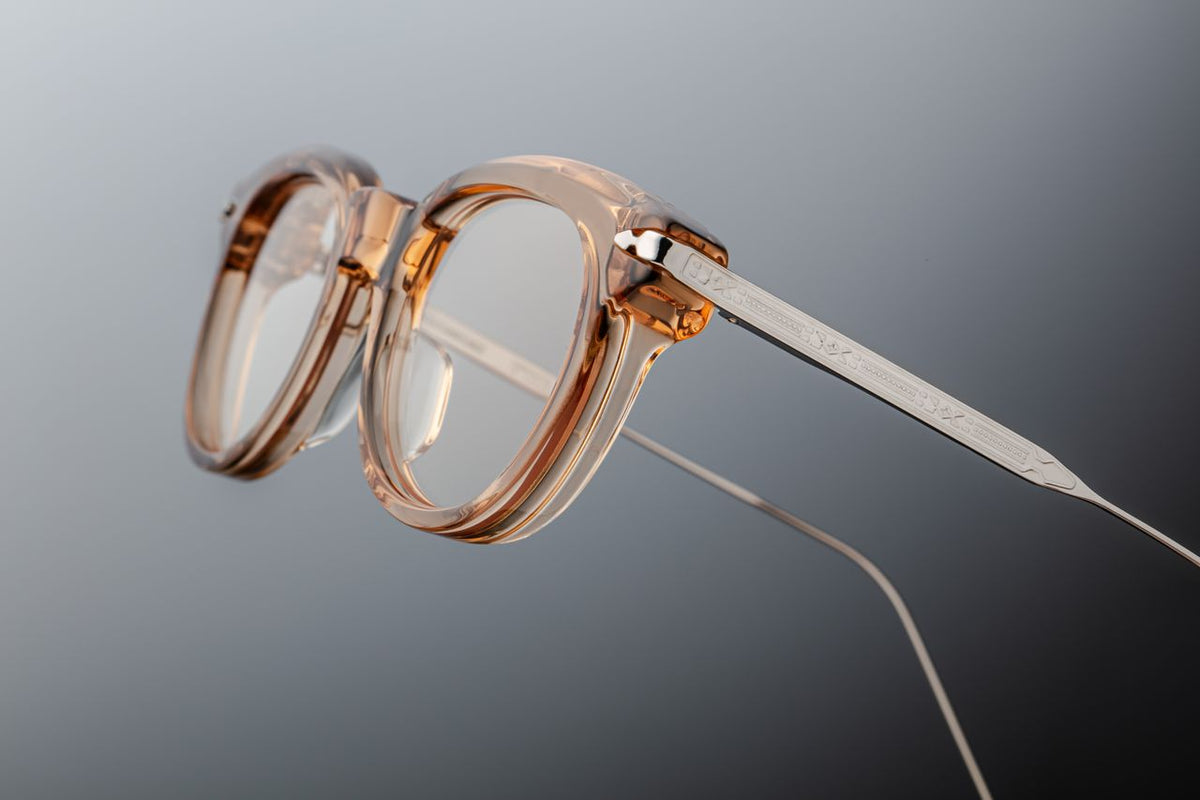 Macro close-up of the Jacques Marie Mage Hisao Sand temple tips from Wink Optometrists. The silver titanium arms transition smoothly into signature hand-painted burgundy epoxy tips