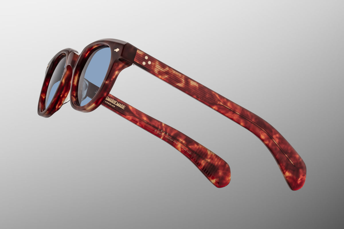 Close-up macro view of the hinge and temple details on the JMM 1948 Breccia frame. Highlights the polished silver palladium 7-barrel hinge, the iconic silver arrowhead pin on the front chassis, and the organic swirls of the brown marbled acetate encasing the custom wirecore.