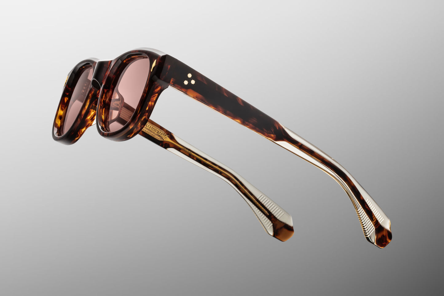 Side view of the JMM Amilcar sunglasses temple arm, showcasing the glossy Havana outer finish, 10k gold spur-shaped rivet heads, and the dark gold wirecores visible through the clear beige inner lining