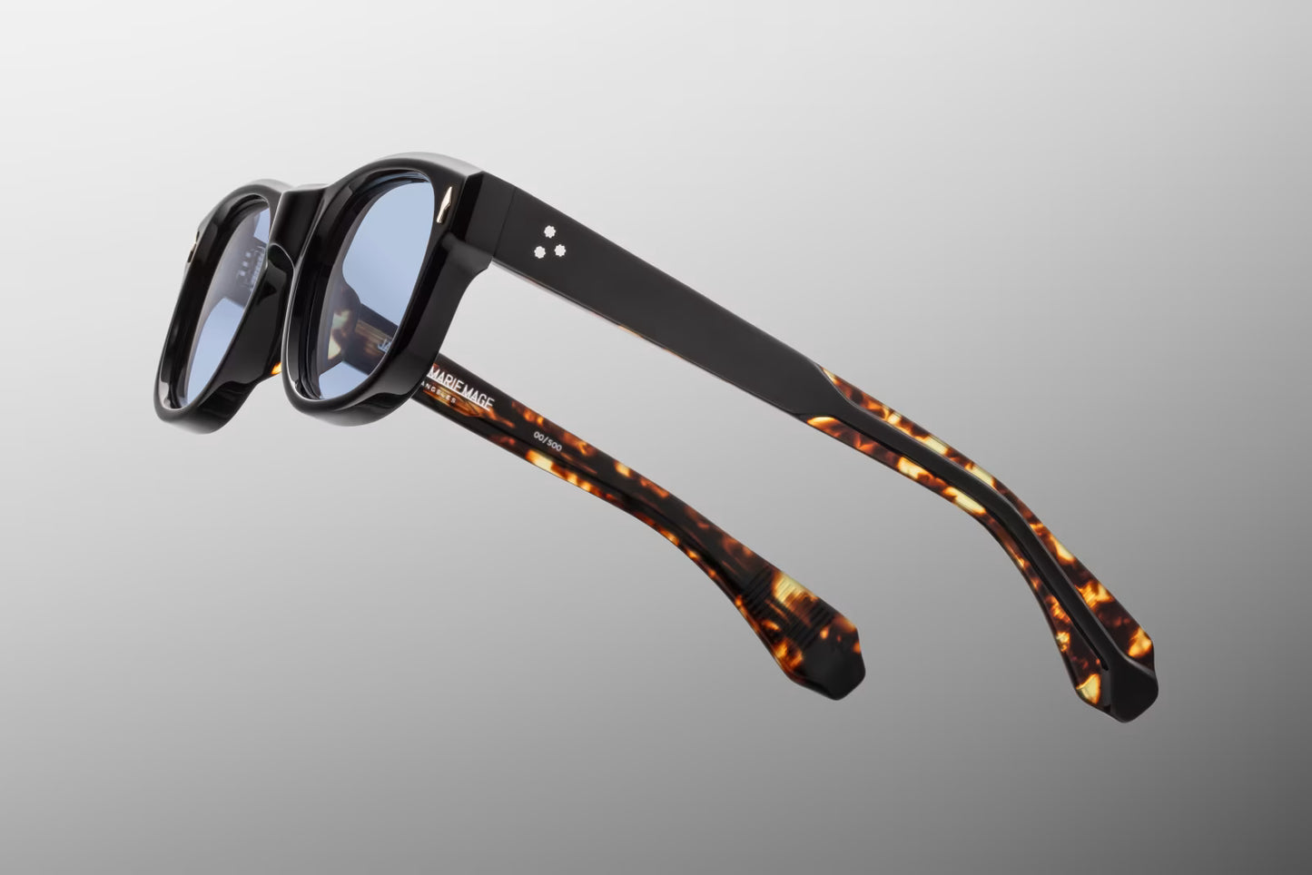 Side view of the JMM Amilcar sunglasses temple arm, showcasing the glossy black outer finish, 10k gold spur-shaped rivet heads, and the exposed dark gold wirecores with custom hairline engravings.