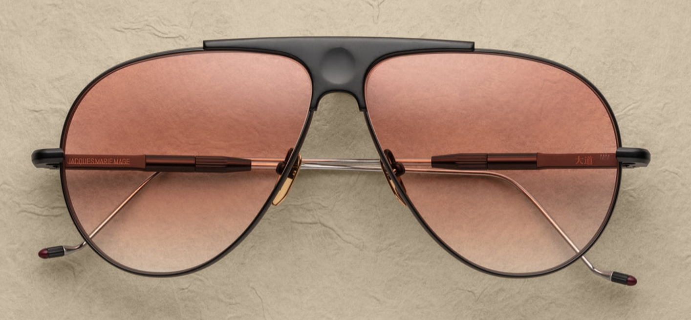 Jacques Marie Mage Daido sunglasses in Black, featuring extendable silver-tone beta titanium temples with burgundy epoxy tips and engraved detailing. The frame includes a distinctive recessed bridge with a circular depression and Art Deco-inspired hairline accents. Handcrafted in Japan, these limited-edition aviators offer 100% UV protection with apricot gradient CR39 lenses and backside anti-reflective treatment