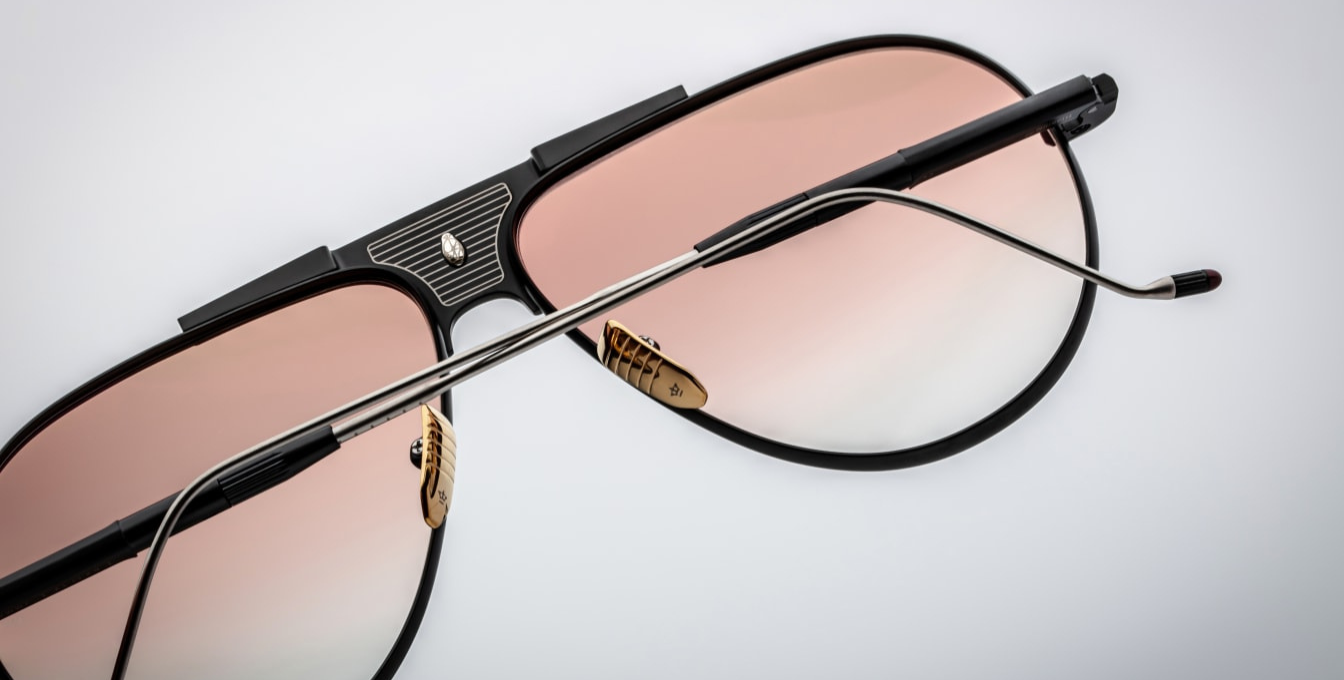 Close-up of the apricot gradient CR39 lenses in Jacques Marie Mage Daido Black sunglasses, offering 100% UV protection and backside anti-reflective treatment. The lenses are set within a sculptural black and silver beta-titanium frame, featuring a distinctive recessed bridge with a circular depression, Art Deco-inspired hairline detailing, and custom dark gold nose pads with engraved insignia.