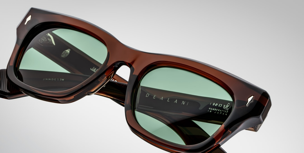 Close-up of the green CR39 lenses of Jacques Marie Mage Dealan sunglasses in Zoltar, offering 100% UV protection and backside anti-reflective treatment. The lenses are set within a 10mm cured cellulose acetate frame, accented with sterling silver arrowhead front pins.