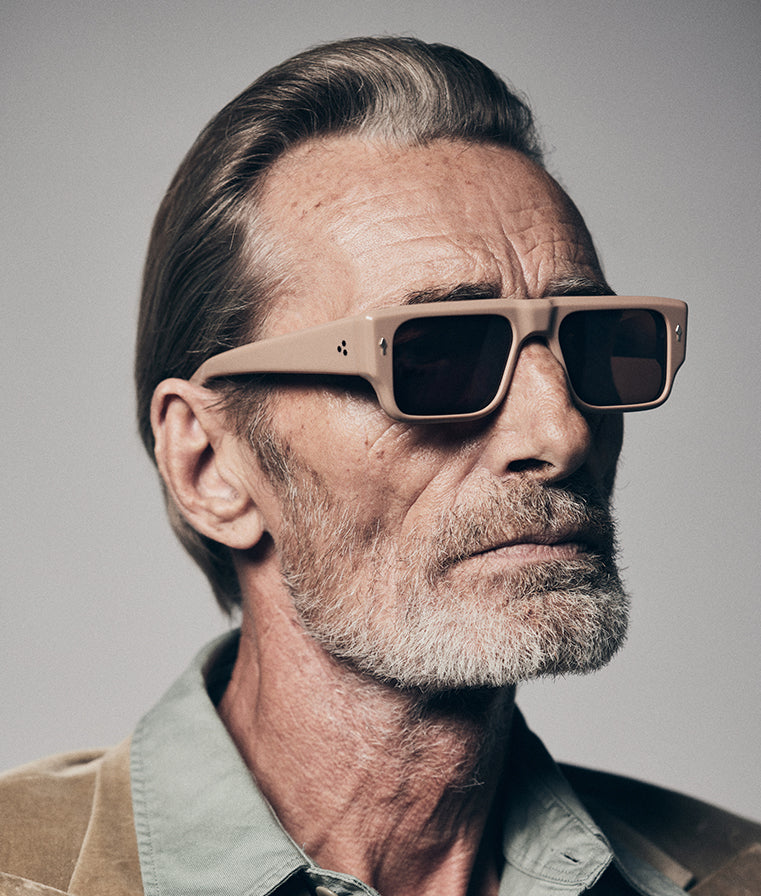 Model wearing Jacques Marie Mage Devoto Porter sunglasses — rectangular brown acetate frame with bold brow‑line, sienna‑brown lenses, profile view
