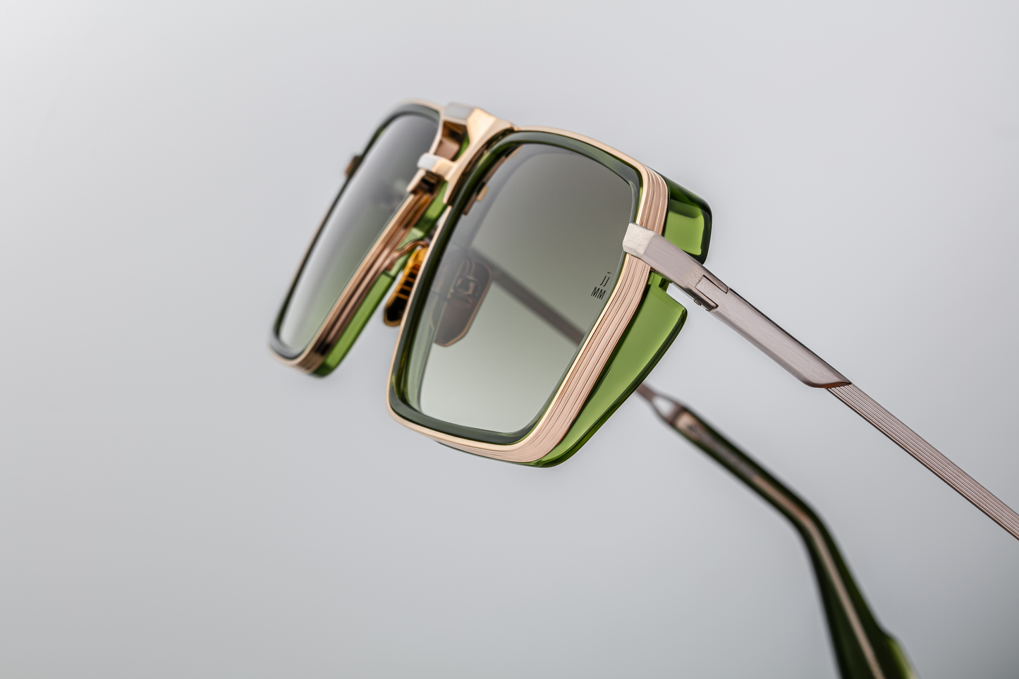 Side‑on view: metal frame transitions to temple arm. The temple is gold, hairline‑engraved, with a green insert near the front, and ends in an acetate tip. Hinge visible, showing solid engineering. The lens front edge shows the thickness and layering (metal + insert).