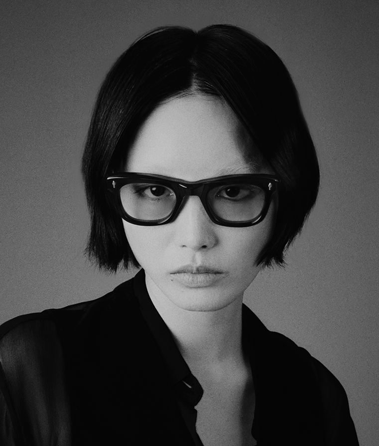 Model wearing Jacques Marie Mage Godard bloodstone eyeglasses, showing the bold silhouette and rich red-brown acetate on face