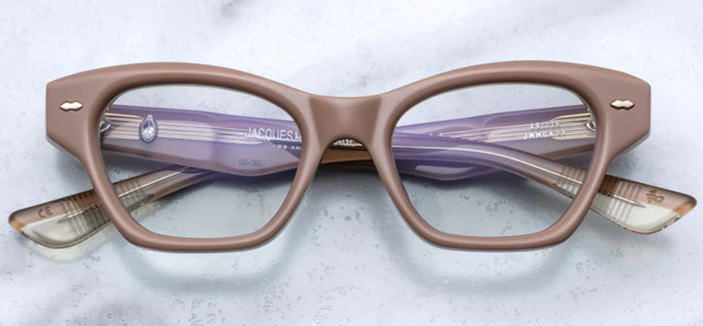 Jacques Marie Mage Grace 2 Porter sunglasses, showcasing a petite cat-eye silhouette with a subtle lift in the eye area. The frame is crafted from 10mm premium Japanese acetate in a soft pink hue, accented with light gold double arrowhead front pins and inner exposed engraved wirecore details. The clear lenses offer a classic optical look