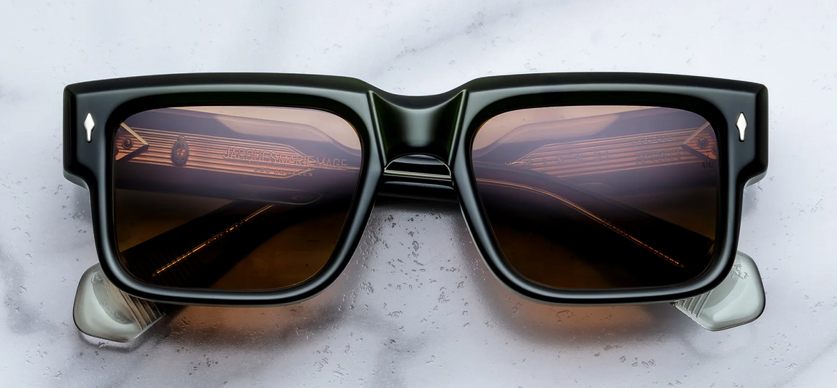 A front-on studio photograph of Jacques Marie Mage Hemmings sunglasses in the limited-edition Borneo colourway. The frames are made from a thick, sculpted, translucent dark bottle-green acetate featuring a bold, 1960s-inspired rectangular silhouette. The distinctively vibrant orange lenses create a sharp contrast against the deep emerald frame. Signature sterling silver arrowhead pins are cleanly inlaid at the top outer corners of the frame front