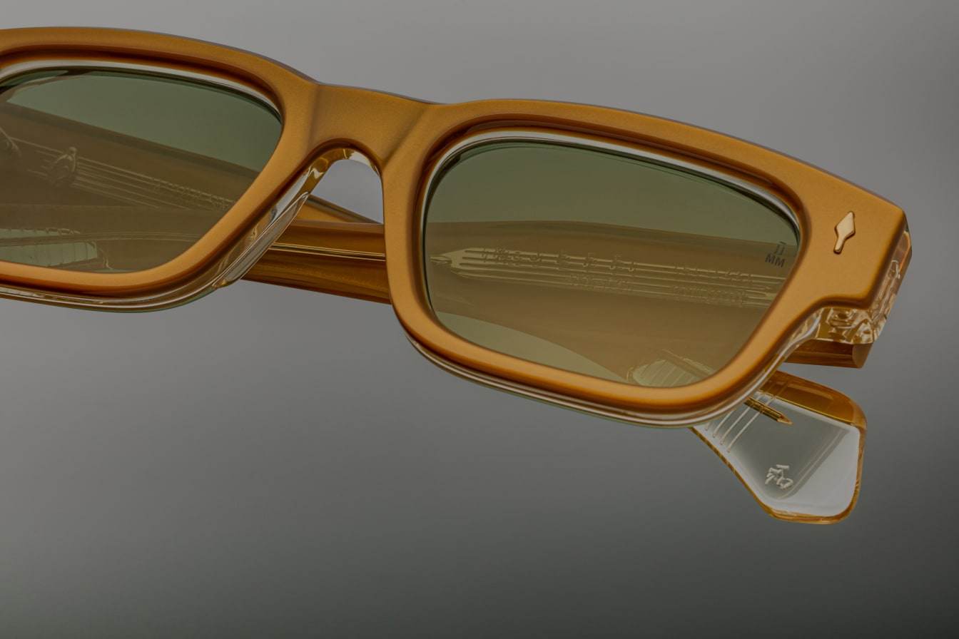 Close-up of the front view of Jacques Marie Mage Jeff sunglasses in Gold, highlighting the bold, round frame made of polished gold-tone metal. Intricate detailing is visible on the bridge and around the lenses, emphasizing the luxurious craftsmanship. The lightly tinted lenses are set within the striking gold frame, giving the sunglasses a vintage-inspired yet contemporary look, with sharp, clean lines that reflect the high-end design. Dark gold arrowhead
