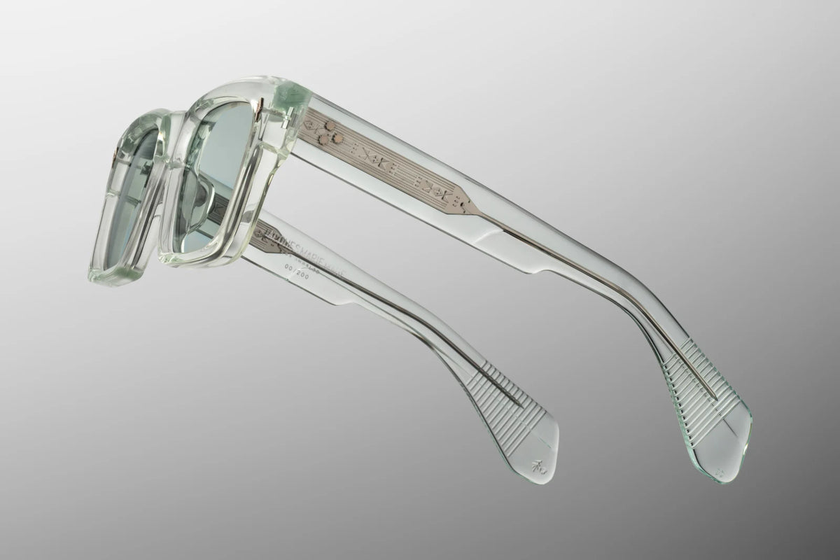 Side profile view of the Jacques Marie Mage Kaine from the Photochromic Collection in Aurora. The focus is on the thick, custom double-laminated temple arms crafted from translucent light green acetate. A premium, tension-secured sterling silver 7-barrel hinge seamlessly attaches the side arms to the translucent front frame face. Available at WINK Optometrists.
