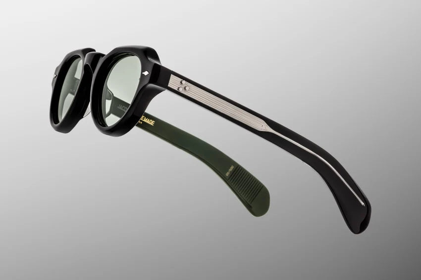 Side profile view of the Jacques Marie Mage Kellerman in Cobra. The focus is on the substantial dual-tone temple arms, which feature a sleek, polished black acetate exterior that transitions cleanly to a vibrant, light bottle green interior laminate layer. A premium sterling silver, tension-secured 7-barrel hinge firmly fastens the temple arm to the black frame face. Available at WINK Optometrists.