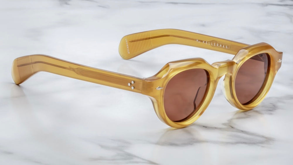 Side profile of Jacques Marie Mage Kellerman Honey sunglasses, highlighting the unique paddle-style temples made from custom acetate. The temples feature light gold hardware and a tension-secured custom 7-barrel hinge, emphasizing the frame's luxurious craftsmanship
