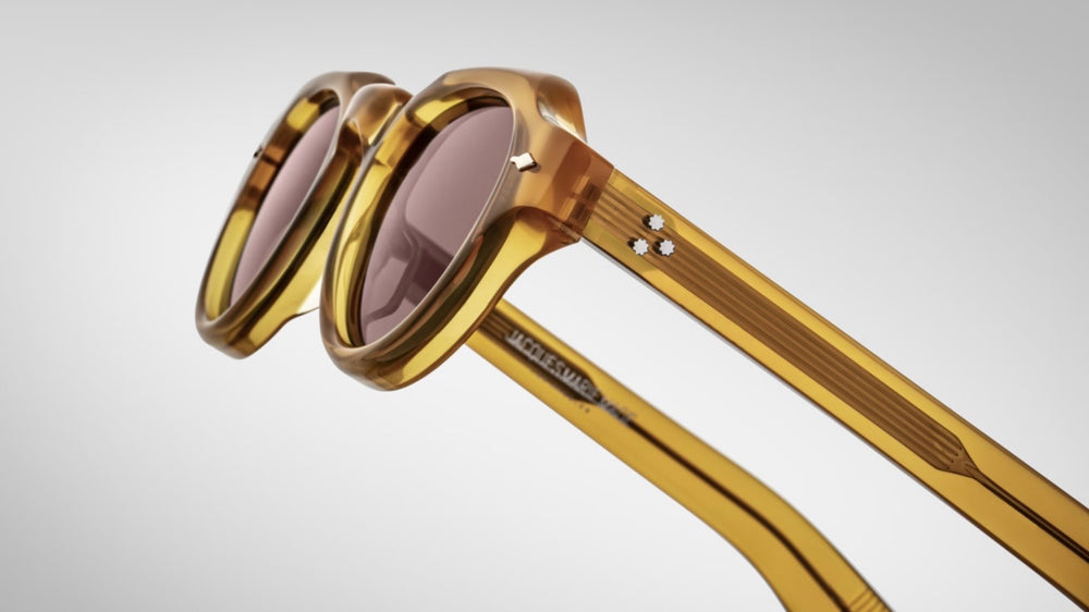 Close-up of the acetate temple tips of Jacques Marie Mage Kellerman Honey sunglasses, featuring light gold metal accents and signature polished metal embellishments. The temples are crafted from custom double-laminated acetate, enhancing the frame's refined aesthetic.