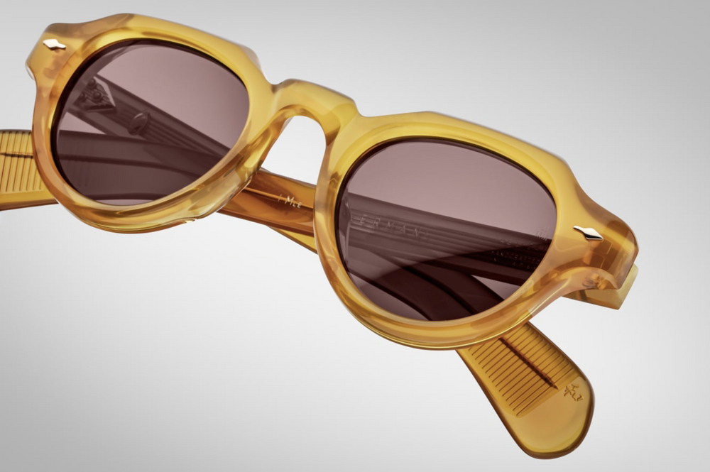 Close-up of the brown CR39 lenses of Jacques Marie Mage Kellerman Honey sunglasses, offering 100% UV protection and backside anti-reflective treatment. The lenses are set within a 10mm cured cellulose acetate frame, accented with light gold arrowhead front pins