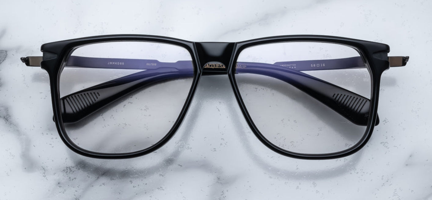 The 70's inspired boxy Kirkland frame by Jacques Marie mage with black cured acetate front, light grey lenses and dark gold 100% beta titanium temples with black accents. Available at WINK Optometrists