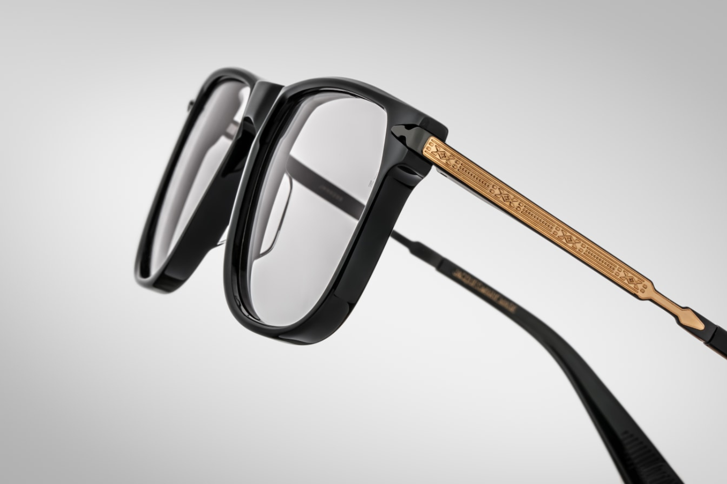 A detailed view of the intricate filigree workmanship in the light gold with silver accents temples in the 70's inspired boxy Kirkland frame by Jacques Marie mage with black cured acetate front, light grey lenses and dark gold 100% beta titanium temples with black accents. Available at WINK Optometrists