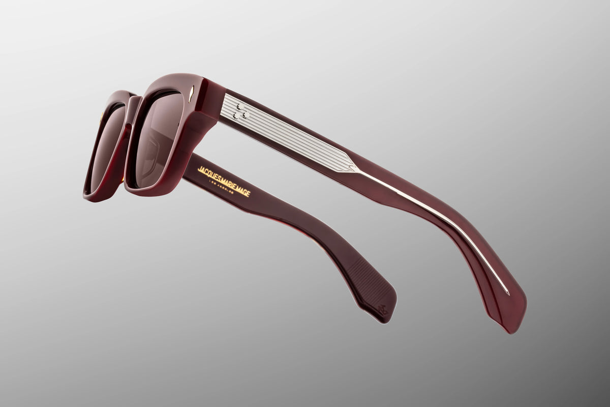 Macro shot of the temple arm on Jacques Marie Mage Molino Bordeaux Empire sunglasses. The crystal-clear outer laminate layer acts as a window to show off the silver palladium wire core engraved with intricate Art Deco filigree.
