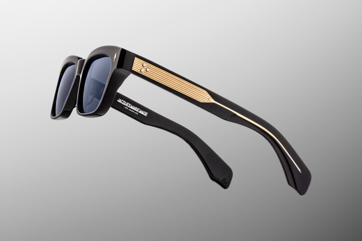Macro shot of the temple arm on Jacques Marie Mage Molino Lacquer sunglasses, showcasing the subtle play of light against the near-black ink-blue acetate and the high-end metallic detailing running through the hinge connection.