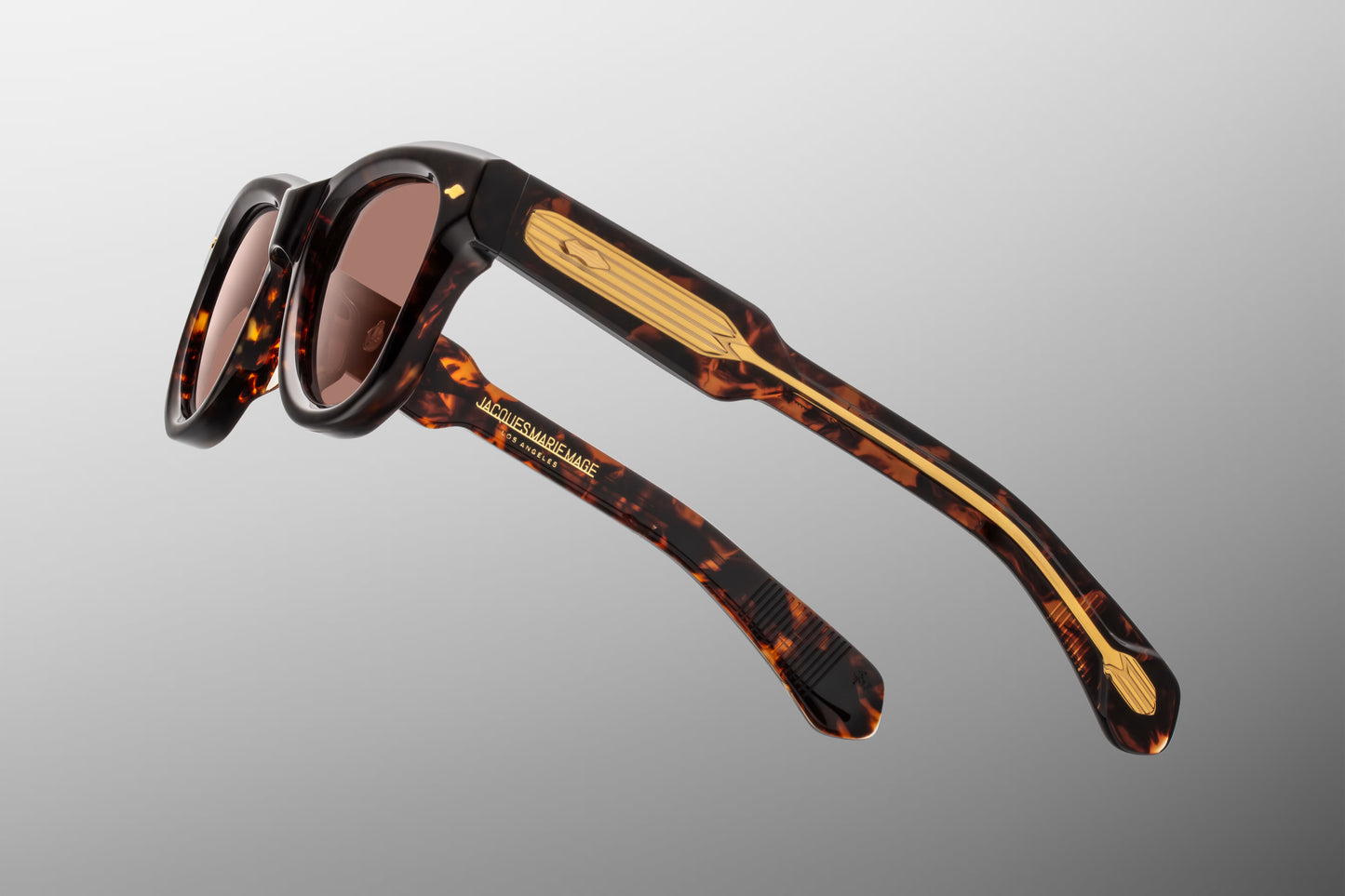 Side view of the JMM Kinshasa sunglasses temple arm, highlighting the clear-beige over dark Havana double-laminated acetate structure and the exposed dark gold wirecore featuring intricate Art Deco hairline engravings