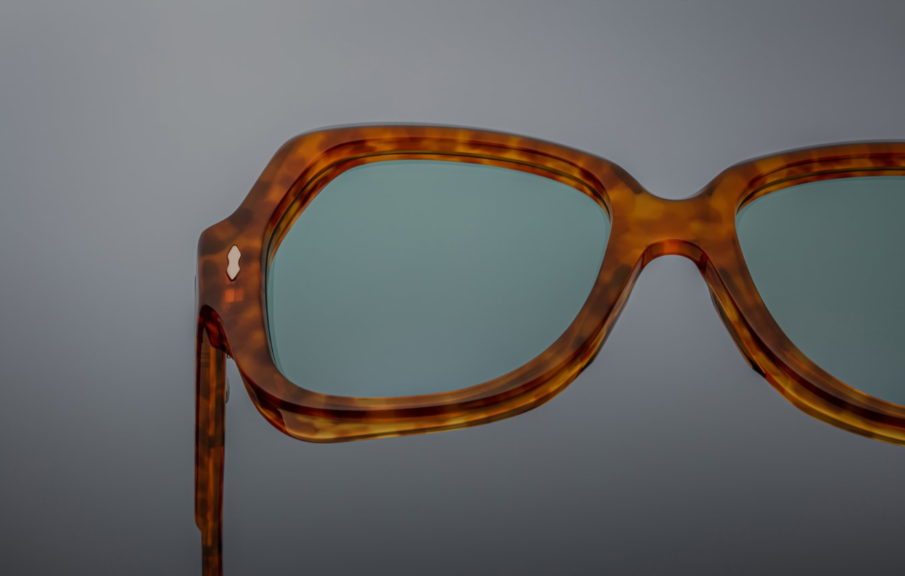 Close-up of the right lens and keyhole bridge area: the clear round CR‑39 demo lens is flush set within the honey-brown acetate rim. The polished bevel edge is crisply finished, and the saddle bridge exhibits smooth curves. A light-gold arrowhead pin peeks into view at the rim’s corner