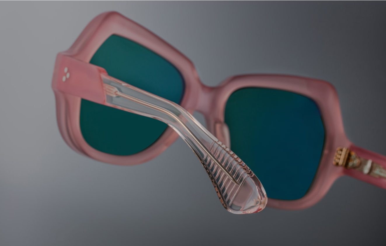 Backside view of the temple: layered pastel pink acetate is visible in cross-section behind the hinge, revealing the internal light‑gold wire‑core. The recessed hinge is secured with matching gold rivets. The temple underside is embossed with ‘54–18–142’, limited‑edition serial number, and ‘Handmade in Japan’ in silver foil.