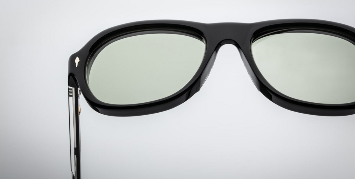 Close-up of the light bottle green CR39 lenses of Jacques Marie Mage Richard Cobra sunglasses, offering 100% UV protection and backside anti-reflective treatment. The lenses are set within a 10mm black cured cellulose acetate frame, accented with sterling silver arrowhead front pins