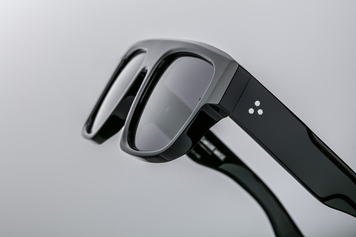 A detailed shot focusing on the temple of the Ritz Noir sunglasses, revealing the custom double-laminated acetate construction with a hidden silver wirecore. The temples feature Jacques Marie Mage's signature arrowhead pin design, adding a unique and recognizable touch.