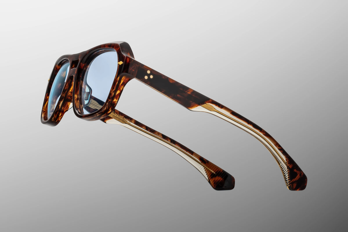 Macro shot of the temple arm on Jacques Marie Mage Tamerlis sunglasses, highlighting the intricate, custom "Cantilever" or "Lever" metal wire core etched with hairline filigree gleaming through a clear laminated acetate layer.