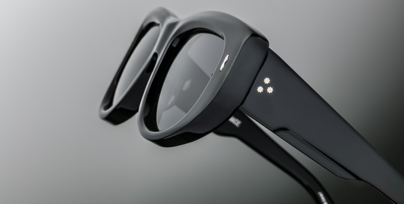 Rivet details for Jacques Marie Mage The Sud | Francoise sunglasses from the Erin Wasson for JMM collection. The sculptural, softly sloped square frame is crafted from 10 mm polished black acetate. It features double-acetate temples enclosing a hidden cantilever silver wire-core, accented with sterling silver double-arrowhead hinge pins, spur-shaped rivets, and Marseille crest temple tips. The lenses are deep jet-gradient CR39 with backside anti-reflective coating and 100%UV protection.