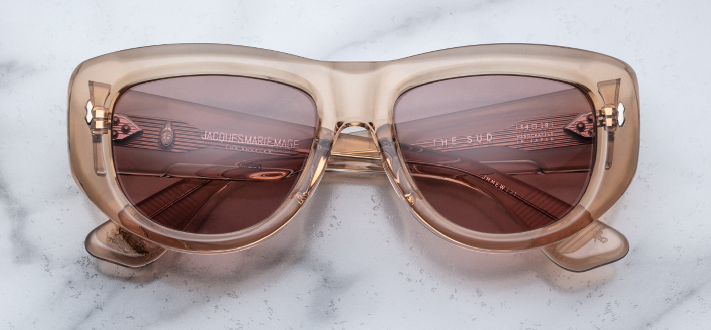 Jacques Marie Mage The Sud | Simone sunglasses from the Erin Wasson x JMM collection in translucent “Clear Sand” acetate. The softly sculpted, 10 mm square-tourer frame features double-laminated temples with exposed cantilevered silver wire-core, secured by tension‑secured 7-barrel hairline hinges. Each hinge front is decorated with sterling silver double-arrowhead pins and spur-shaped rivets. Bronze‑tinted CR39 lenses with a 6‑base curve, backside anti-reflective coating, and 100 % UV protection.