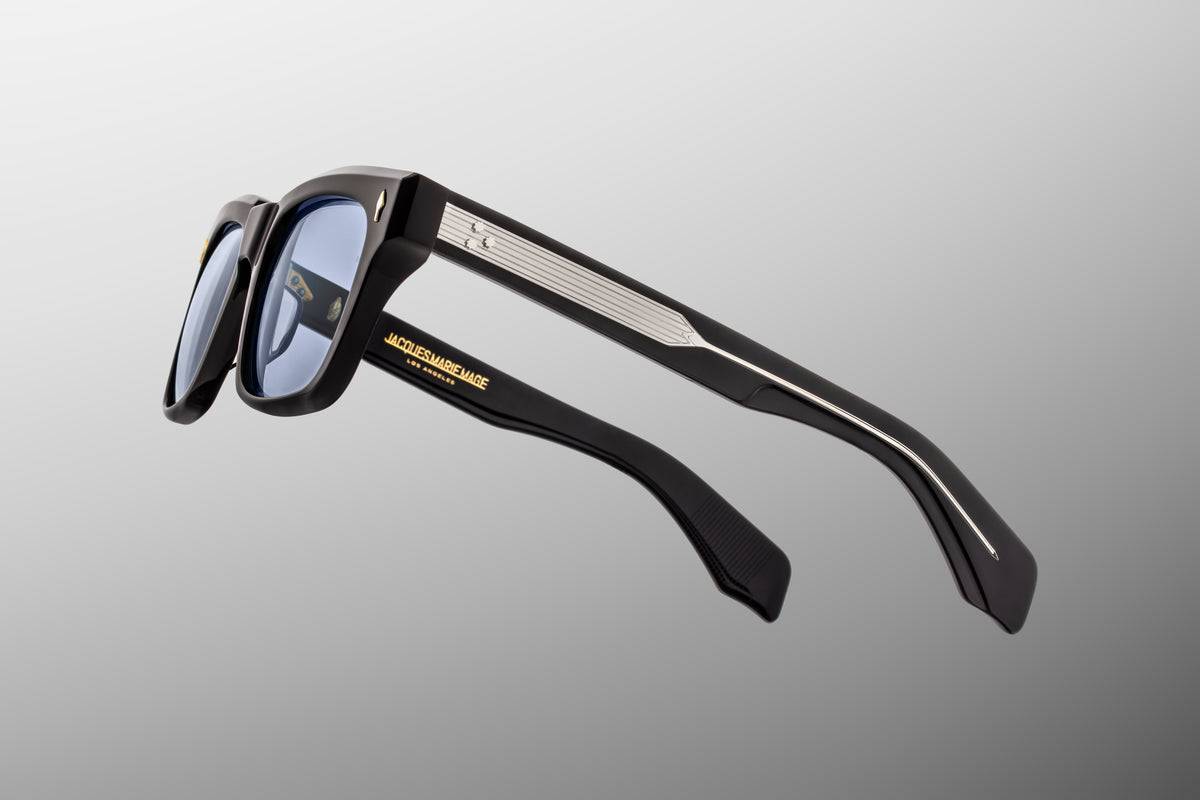 Macro shot of the inner temple arm on Jacques Marie Mage Torino Obscure sunglasses. The crystal-clear interior laminate layer provides a window to the exposed dark gold wire core engraved with intricate hairline filigree.