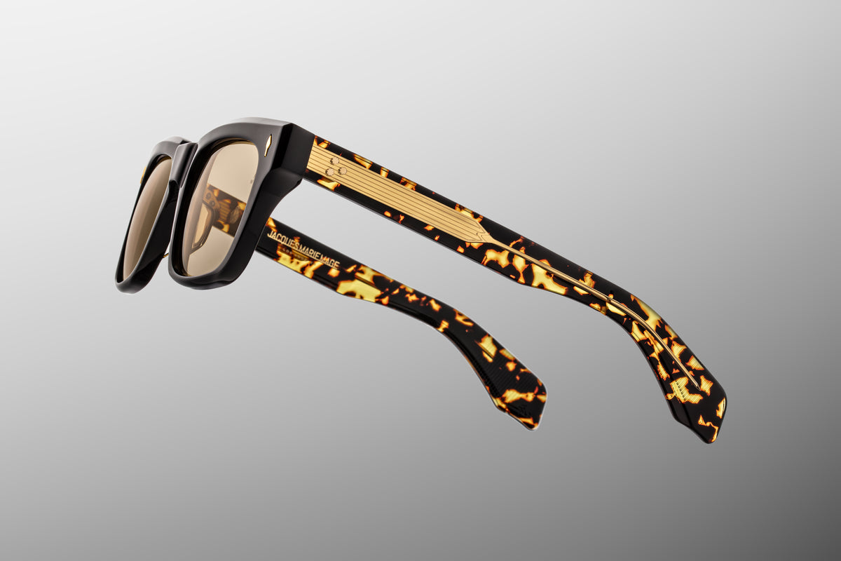 Macro shot of the inner temple arm on Jacques Marie Mage Torino Tavern sunglasses. The crystal-clear interior laminate layer provides a window to the exposed dark gold wire core engraved with intricate hairline filigree.
