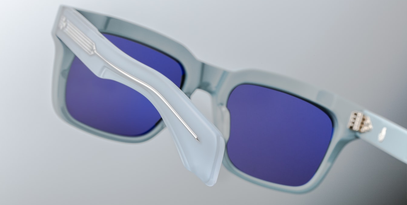 Back view of JMM Molino Tiger sunglasses — polished blue acetate temples with exposed silver core, engraved wire-core, and the silver 7-barrel hinge visible beneath the double-laminated acetate.