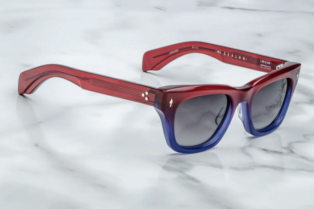Side profile of Jacques Marie Mage Dealan sunglasses in Vesper, featuring a flared square frame crafted from 10mm cured cellulose acetate in a red-to-blue gradient. The design includes custom double-laminated acetate temples, silver arrowhead front pins, and tension-secured monoblock hinges. The jet gradient CR39 lenses offer 100% UV protection and backside anti-reflective treatment. Handcrafted in Japan, this limited-edition model is part of a 350-piece production run, combining bold volumes and sleek line