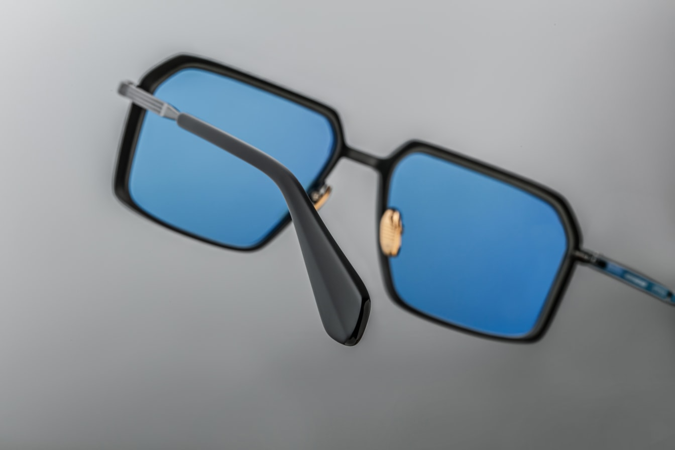Close-up of the blue CR39 lenses of Jacques Marie Mage Vasco sunglasses, offering 100% UV protection and backside anti-reflective treatment. The lenses are set within a black beta titanium frame with sculpted volume cuts and hairline epoxy detailing. Available at WINK Optometrists