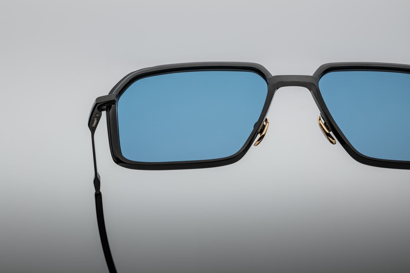 Close-up of the blue CR39 lenses of Jacques Marie Mage Vasco sunglasses, offering 100% UV protection and backside anti-reflective treatment. The lenses are set within a black beta titanium frame with sculpted volume cuts and hairline epoxy detailing.