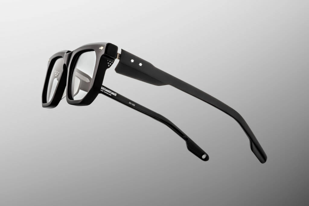 Side profile view of the Jacques Marie Mage Yoshi in Black. The focus is on the thick, custom-sculpted black acetate temple arms. A premium, high-polish sterling silver tension-secured multi-barrel hinge seamlessly attaches the side arms to the deep black frame face, creating a striking contrast with the glossy black surface. Available at WINK Optometrists.