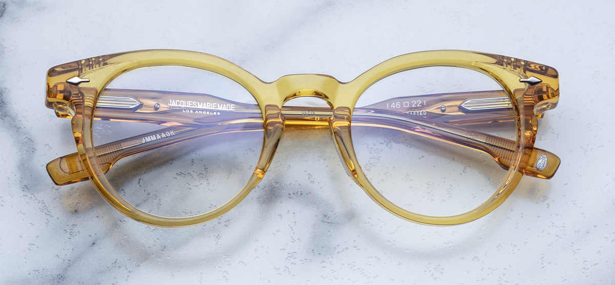 Front view of the limited-edition Jacques Marie Mage Arp eyeglasses in Seed, available at Wink Optometrists. Part of an exclusive global batch of 350 pieces, the unisex panto-shaped frame features a bold, 12mm block of translucent dark yellow acetate with a classic keyhole bridge and signature Sterling Silver arrowhead front pins.

