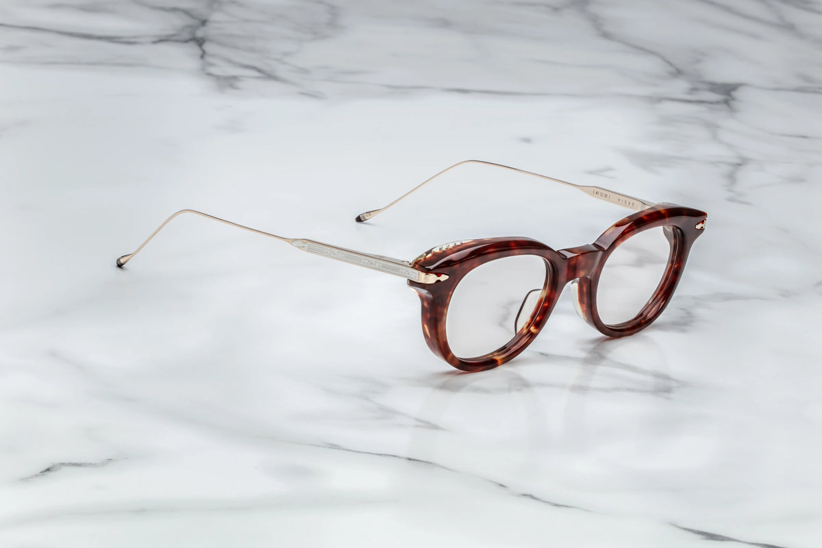 A three-quarter angled view of the Jacques Marie Mage Hisao Breccia frames, available at Wink Optometrists. The perspective highlights the substantial depth of the brown acetate front alongside the custom, tension-secured monoblock hinges.