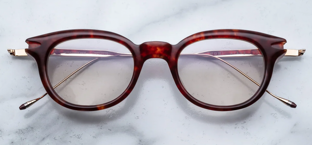 Front view of Jacques Marie Mage Hisao eyeglasses in Breccia, available at Wink Optometrists. The panto-shaped frame features a thick, rich brown cured cellulose acetate front with a distinctive keyhole bridge and gold arrowhead accents.