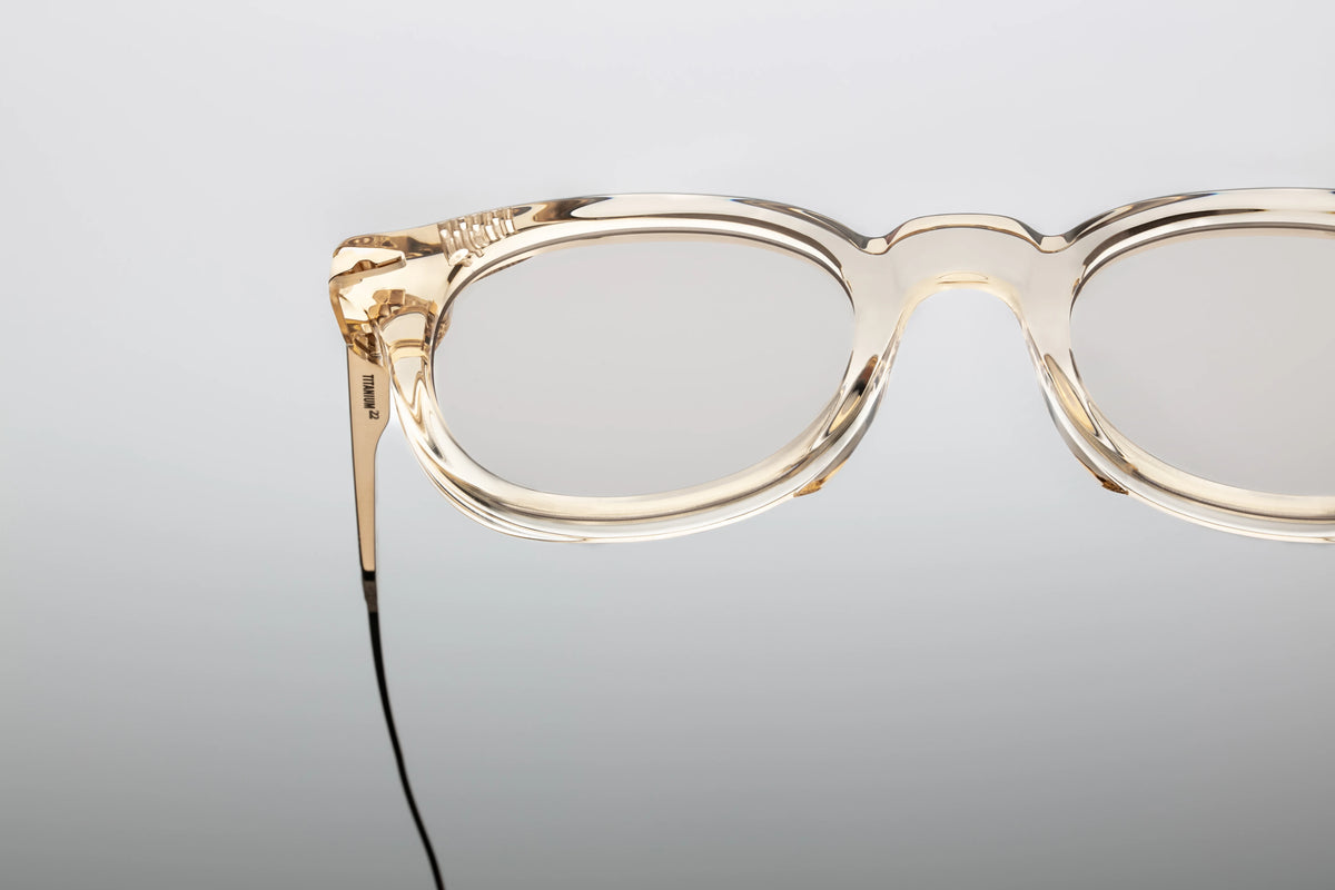  Macro close-up of the front face of the Jacques Marie Mage Hisao Pearl frame, focusing on the endpiece. The highly polished, ice-like transparency of the thick cured acetate catches the light, perfectly encasing the polished sterling silver arrowhead pin. The edge reveals clean, hand-finished structural contours where the frame transitions down toward the lens rim.