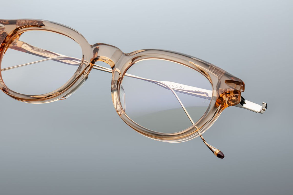  A macro close-up of the Jacques Marie Mage Hisao Sand hinge mechanism, showcasing the luxury eyewear available at Wink Optometrists. The shot reveals the precision floating hinge system connecting the tan acetate front to the engraved silver titanium arm.