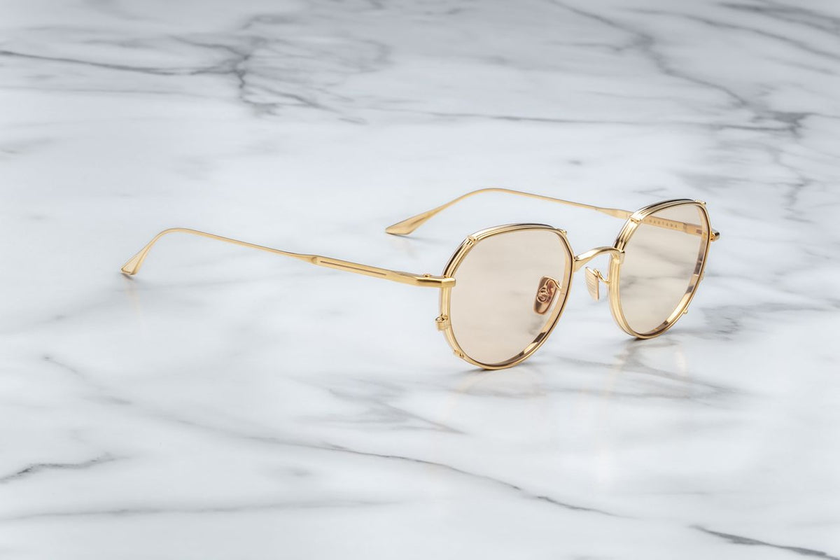 A three-quarter angled view of the Jacques Marie Mage Hartana Gold frames, available at Wink Optometrists. The dynamic perspective captures the depth of the structural double eyerim, the custom gold hidden hinges, and the subtle Dark Tuscan tinted lenses