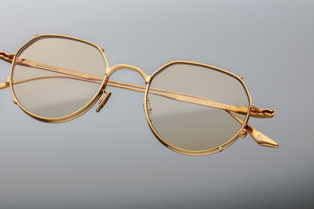 A macro close-up of the delicate nose bridge hardware on the Jacques Marie Mage Hartana Gold glasses, showcasing artisanal luxury at Wink Optometrists. The shot details the pure light gold titanium nose pads featuring precision hairline engravings and the official JMM crest logo