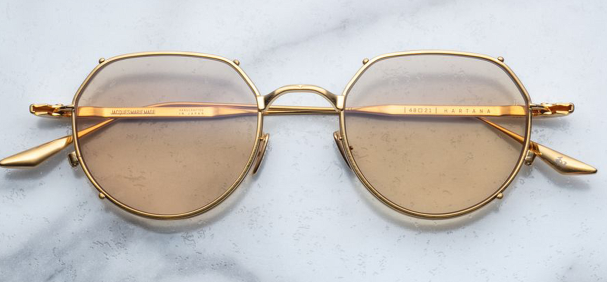 Front view of the limited-edition Jacques Marie Mage Hartana eyeglasses in Gold, available at Wink Optometrists. Part of an exclusive batch of 500 pieces, the panto-shaped frame features a lightweight, light gold 100% beta titanium construction with a prominent double-layered lens rim that gives a classic clip-on effect.

