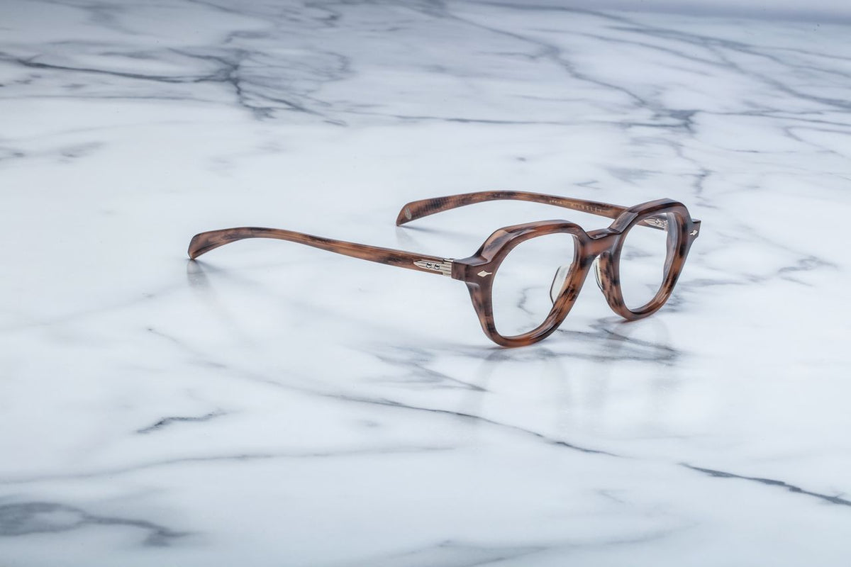 Side profile view of Jacques Marie Mage Insley glasses in Oak. The thick, custom double-laminated acetate temple arm showcases a prominent brown-streaked finish. A custom hairline-engraved, light-gold wire core is clearly visible through the translucent frame material, extending toward a temple tip finished with a subtle 3D metal cameo logo
