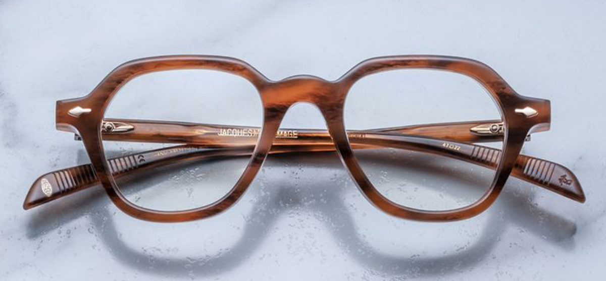 Front view of Jacques Marie Mage Insley glasses in Oak. The frame features a chunky, 10mm-thick cured cellulose acetate construction with a brown-streaked, polished oak wood-grain finish. It features a classic, softly rounded square silhouette, a structured bridge, and signature light-gold arrowhead front pins embedded near the upper corners