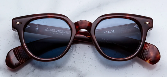 Front view of Jacques Marie Mage Stanley Kubrick 1948 sunglasses in Breccia. Features a bold, thick, rounded mid-century acetate frame with a striking marbled dark brown and Havana texture. Includes a structured keyhole nose bridge, signature sterling silver arrowhead front pins, and rich Prussian blue lenses