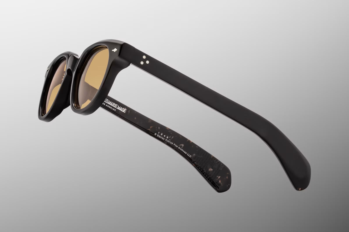 Close-up macro view of the hinge and temple of the JMM 1948 Willow frame. Highlights the polished silver palladium 7-barrel hinge, the iconic silver arrowhead pin on the front chassis, and the intricate filmography-inspired motifs engraved on the custom Kubrick wirecore.
